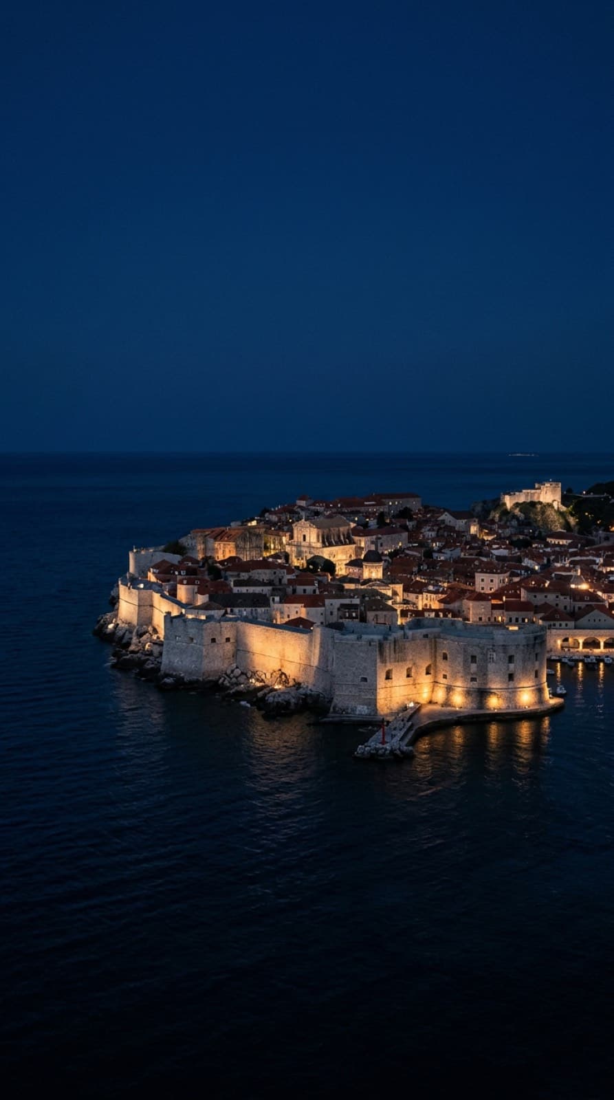 Una ciudad amurallada de la costa dálmata al anochecer, con el Adriático oscuro al fondo