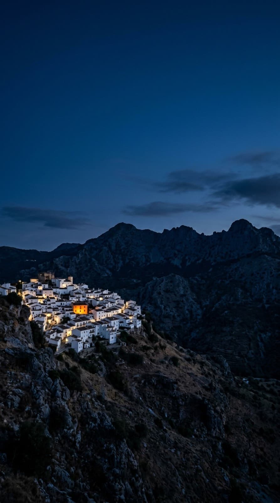 Un pueblo blanco andaluz al anochecer, encaramado a una ladera con las luces encendidas