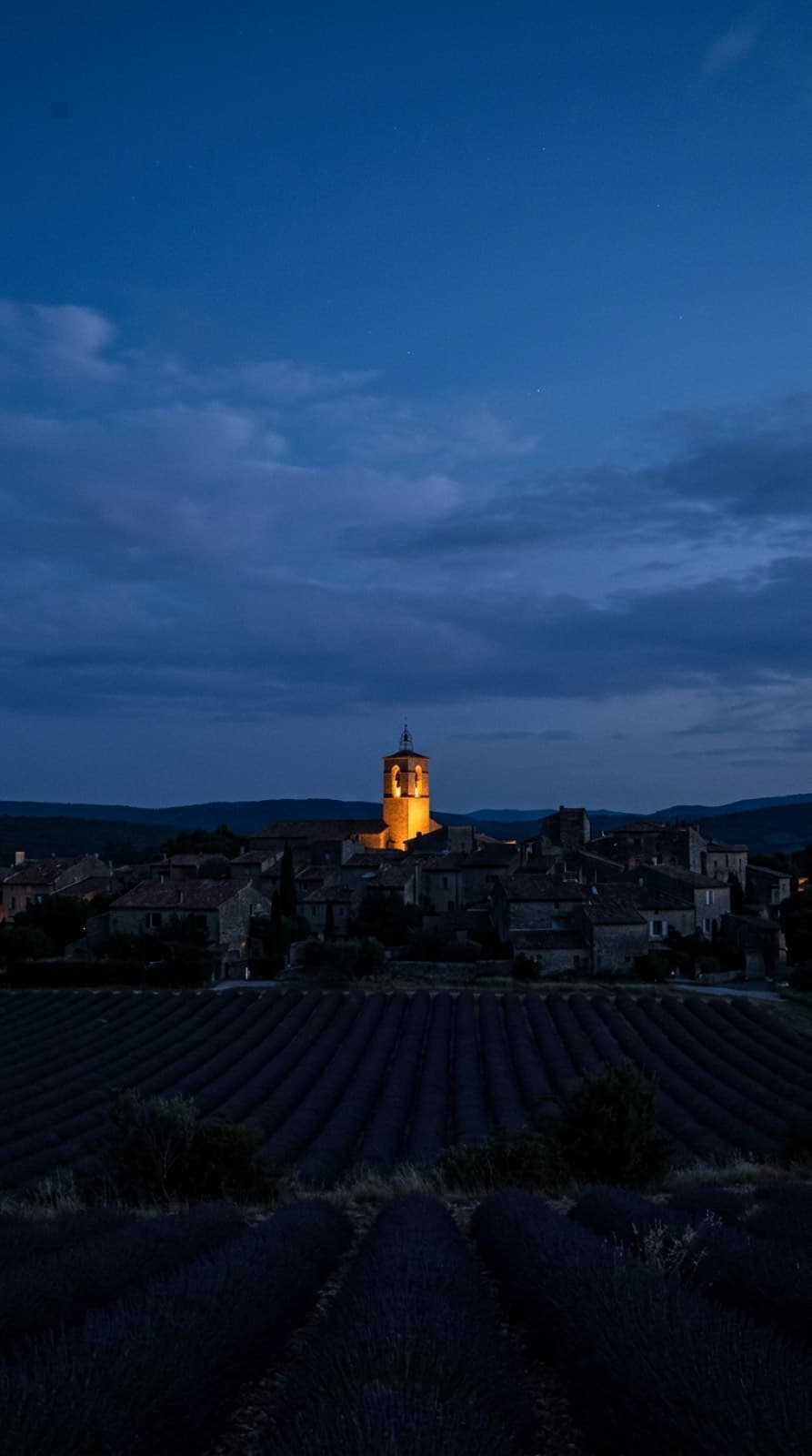 Un pueblo de la campiña francesa al anochecer, con el campanario iluminado sobre los tejados