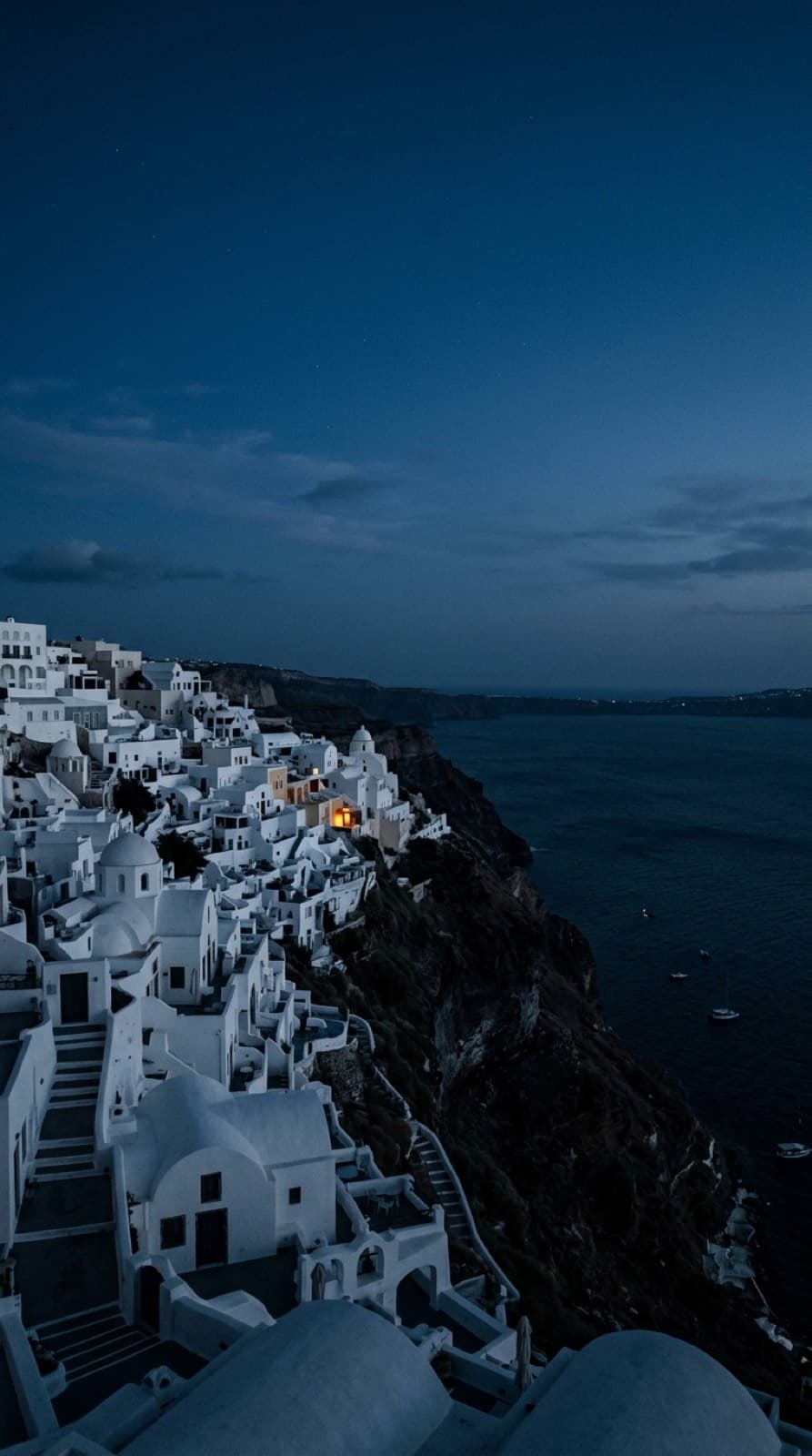 Un pueblo de las islas griegas al anochecer, casas blancas escalonadas sobre el mar oscuro