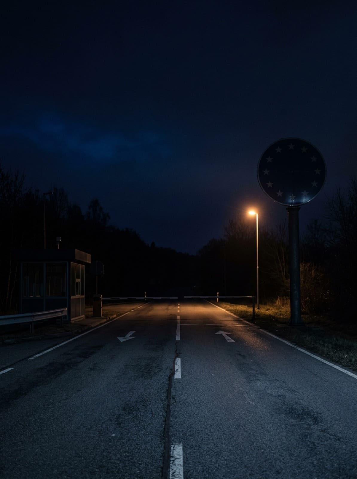 Un paso fronterizo europeo de noche, con la carretera siguiendo hacia la oscuridad