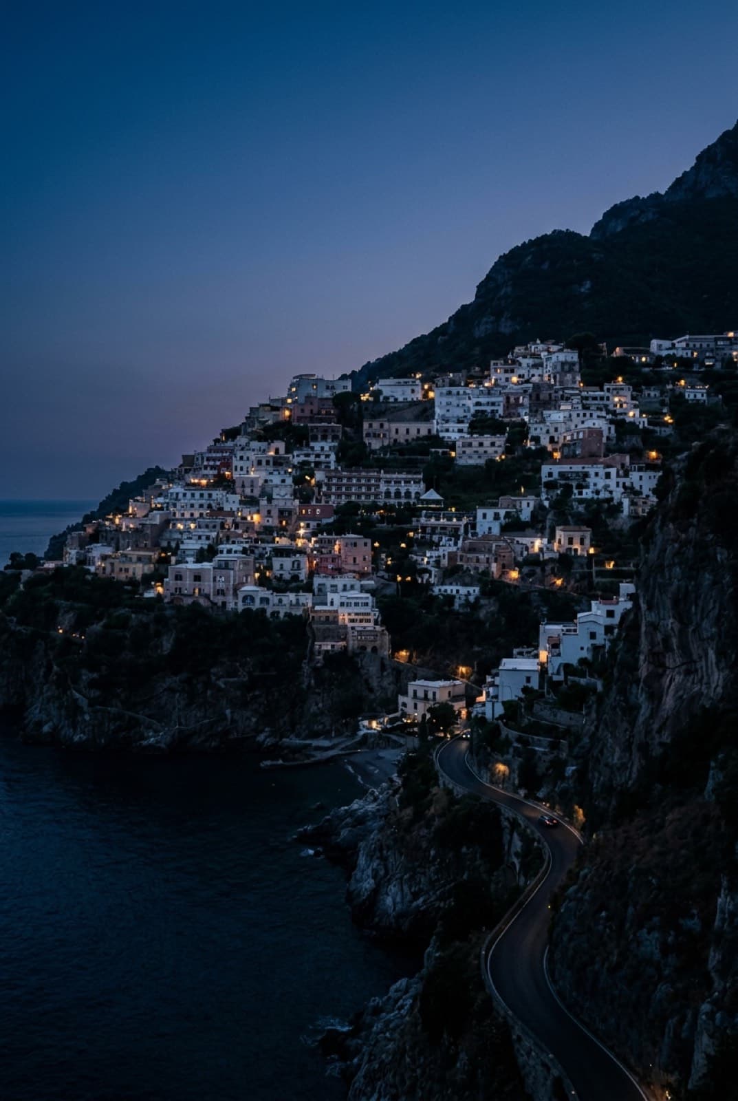 Un pueblo de la costa italiana al anochecer, con las luces encendidas sobre el acantilado